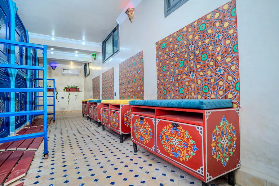 Un couloir avec des cabines bleues d'un côté et des banquettes rouges peintes sous des panneaux géométriques
