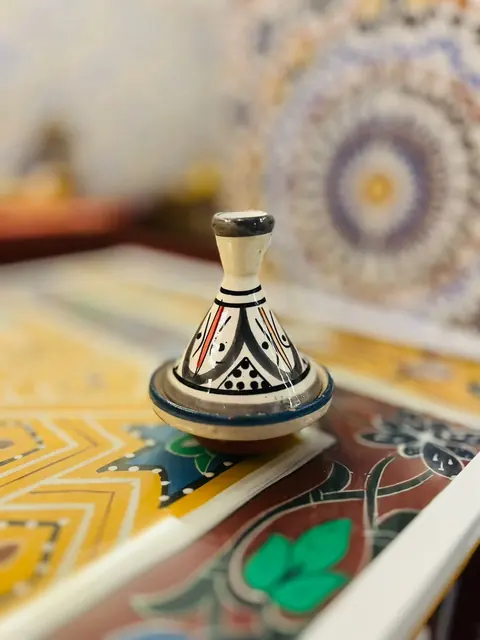 Un petit tajine en céramique peint à la main, posé sur des plateaux décorés