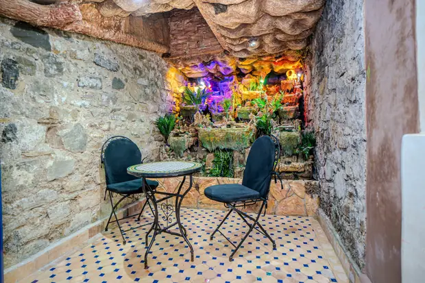 Un patio en pierre avec une petite table en mosaïque, deux chaises et une fontaine de rocaille éclairée