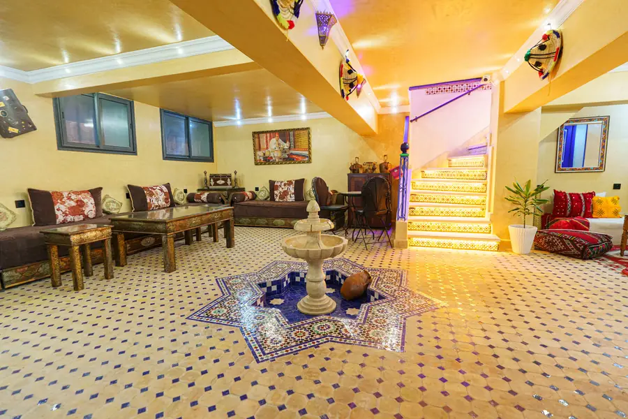 Le grand salon : banquettes marocaines, tables basses, fontaine centrale et sol en zellige